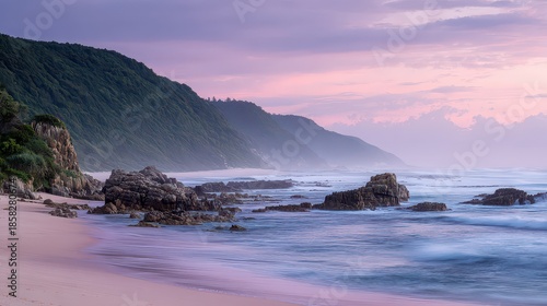 Serene Coastal Scenery with Lush Green Hills Sandy Beach and Rocky Outcrops Under a Pastel Colored Sky in Soft Lighting with Mist and Calm Waters