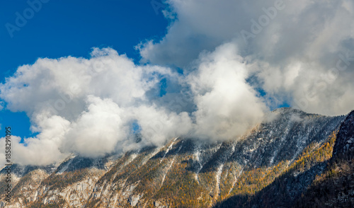 Dramatic white clouds cling to the rugged, snow-dusted peaks of the Austrian Alps above Hallstatt.