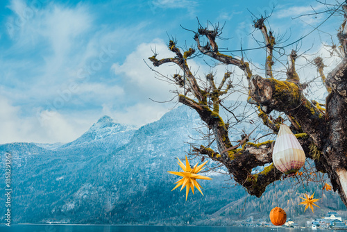 Golden Moravian stars and lanterns hang from a mossy tree overlooking the snowy peaks and still waters of Hallstatt Lake.