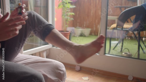white man applying bandage to foot wound near balcony, cleaning and dressing with gauze and tape while using antiseptic steady first aid sequence and home medical care after minor