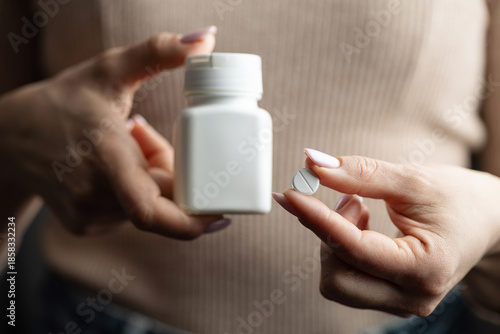 Foto Close-up of female hands holding white pill bottle and single white round pill w