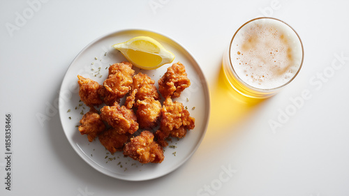 真上から白い皿に唐揚げを配し、白背景でビールとレモンを整然と置いた昼
