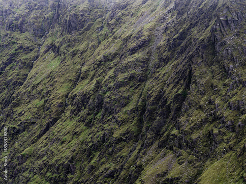 A steep mountainside features green moss growing on rocks. Grey cliffs and ravines cut through the terrain.
