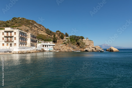 Coastal buildings of Therma village facing calm blue waters on Ikaria island, Greece. Peaceful Mediterranean scenery and wellness destination near natural hot springs.