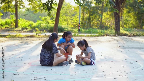 Asian mother and daughters sitting on court, resting and talking after playing basketball.