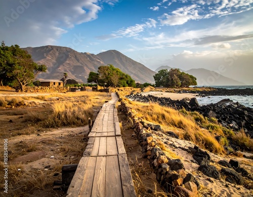 Wooden boardwalk leads to a rocky beach, distant mountains under a vibrant blue sky with scattered clouds