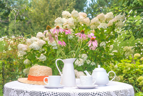 Two white cups of tea, tea pot, bouquet of pink flowers on a table in a blooming garden