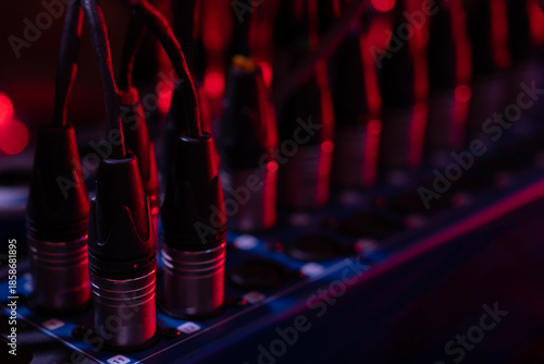 Multichannel audio snake cables plugging into a stage box, processing sound signals for live concert production and broadcasting, illuminated by red stage lights