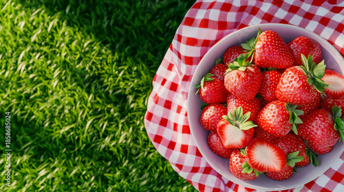A bowl of strawberries on an outdoor table, with some strawberry slices and a red-and-white checkered cloth beside it, creating a fresh atmosphere.
