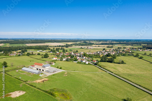 Obraz na plátně Aerial view of Saint-Germain-Chassenay showing farm buildings, green fields, and a clustered rural village under a vivid blue sky