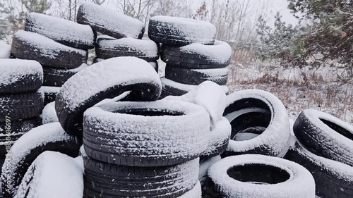 Stacking used car tires covered with fresh snow outdoors. Piles of old automobile tires accumulating snow in winter storage yard during snowfall