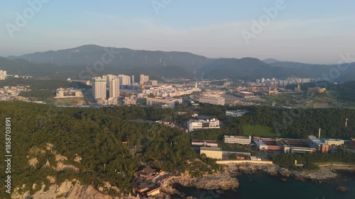 Panoramic aerial perspective captures South Korea's coastal beauty, blending the serene Haedong Yonggungsa Temple on rocky shores with a bustling city, modern high-rises, and a vibrant leisure park se