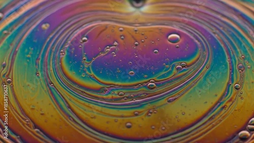 A macro shot displays colorful, iridescent patterns on a bubbly, textured surface. Bubbles dance