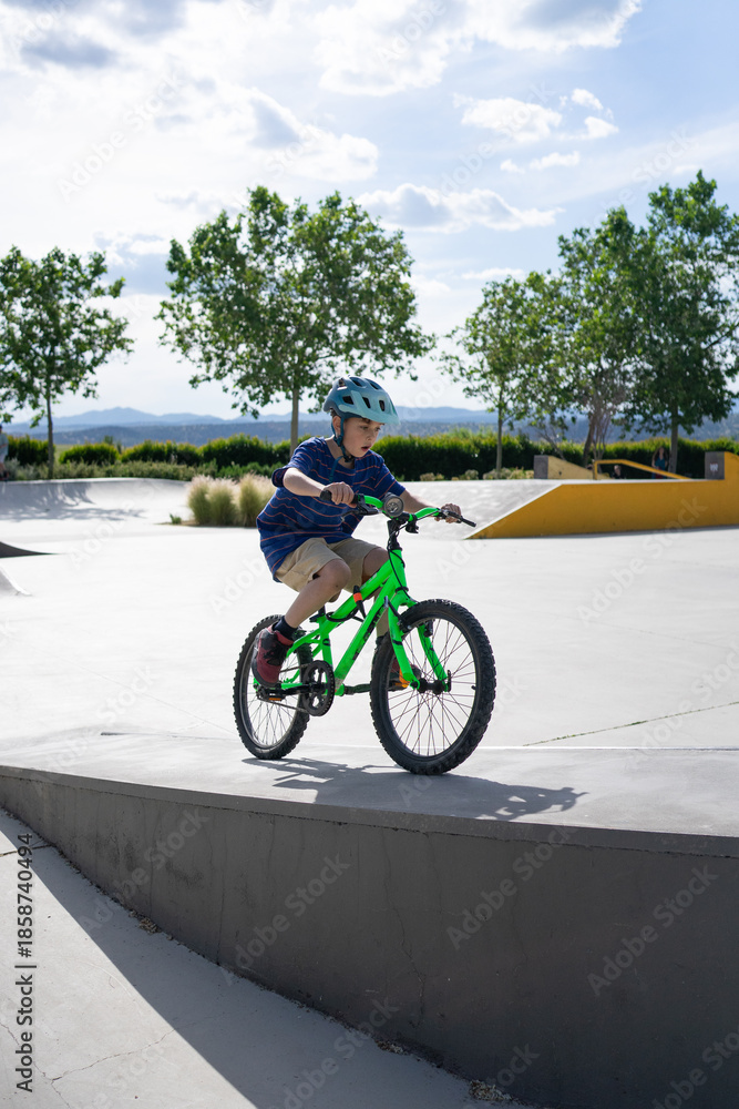 Obraz premium Child cyclist practicing in skate park during summer sunny day
