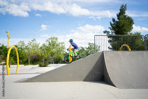 Canvas Print Young boy riding bike up ramp in skatepark on sunny day