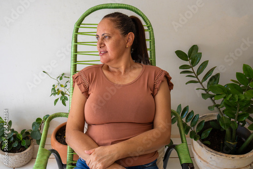 Mature woman relaxing at home sitting on chair surrounded by plants