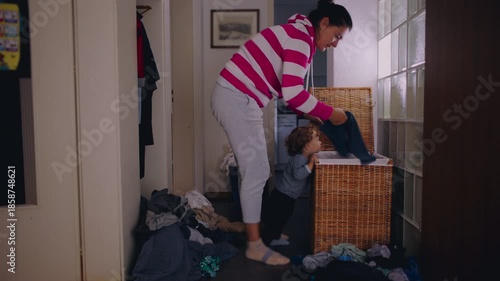 Mother sorting laundry from basket while toddler stands nearby watching movement showing everyday caregiving routine and quiet domestic life at home