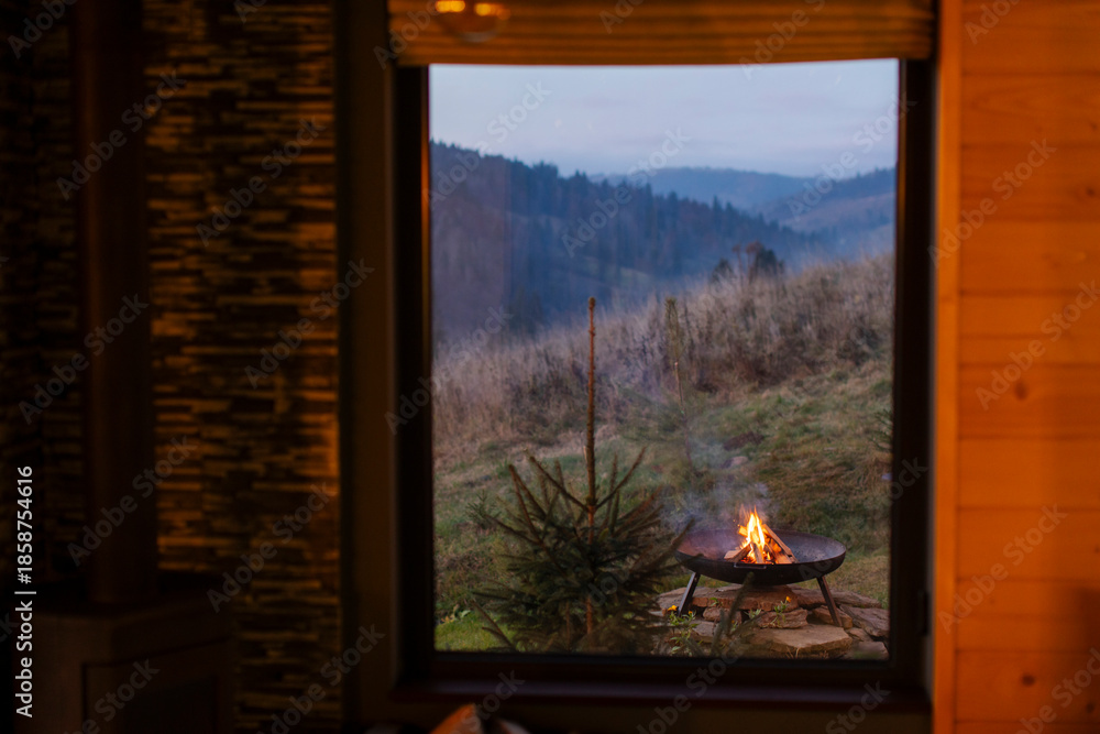 Fototapeta premium Fire pit outside cabin, view form window on mountains and backyard in the evening