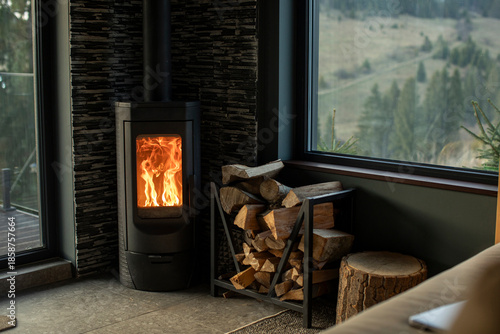 Schilderij op canvas Wood stove burning brightly in the corner of room, stacked logs placed next to s