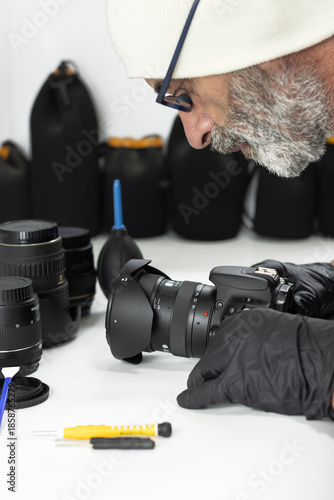 Technician inspecting DSLR camera with lens using precision tools in studio. Concept of camera repair service, photography maintenance, optical equipment care, professional technology support.
