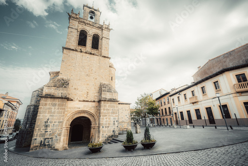 Stone church tower and entrance on quiet town square in Salas, Asturias, Spain, along Camino de Santiago Primitivo route; historic stone architecture, cobblestone pavement, cloudy sky, copy space
