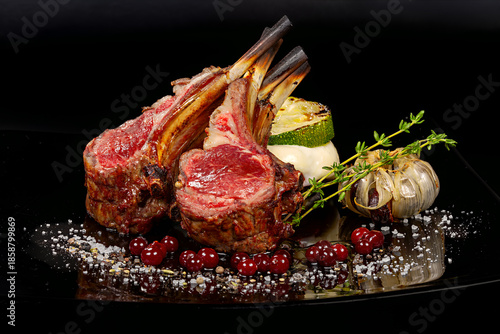 Rack of Lamb - The meat is cooked to medium rare, giving it a pink hue and a tender texture. The dish is garnished with roasted garlic, red currants, and a sprig of rosemary
