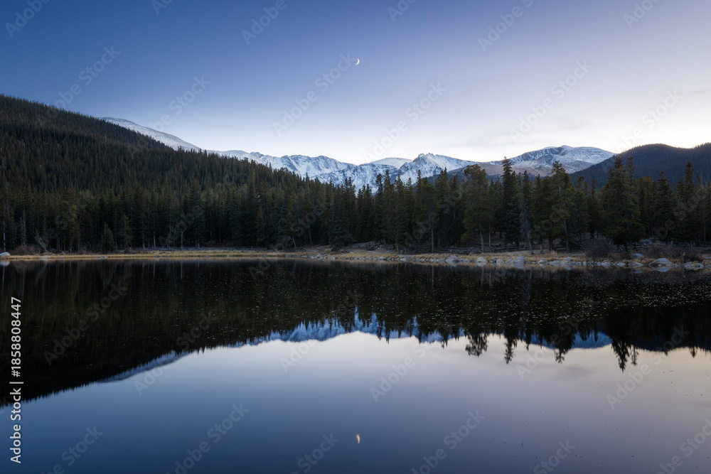Fototapeta premium Snow mountain reflection with a crescent moon at dusk on Echo lake Idaho Springs, Colorado