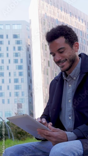 Vertical HD video of young adult businessman working on tablet at city park. Productive moment blending technology and nature. Business and people concept.