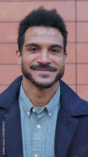 Vertical HD video portrait of young adult Latin American man smiling in outdoor portrait. Confident professional posing against minimalist wall background. Lifestyle and wellbeing concept.