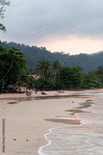 Waves gently lap at the sandy shore as palm trees sway in a tropical breeze at twilight.