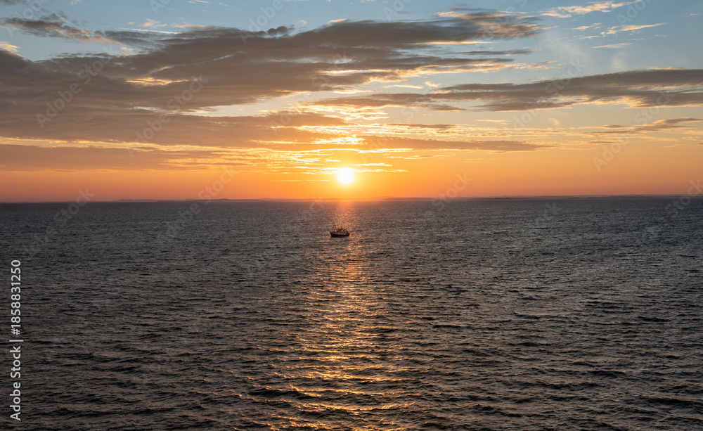 Fototapeta premium A fishing boat sails in the warm morning sunbeam through the Norwegian Sea at sunrise. Warm morning light shines over the water, creating a bright scene for shrimp fishing. 