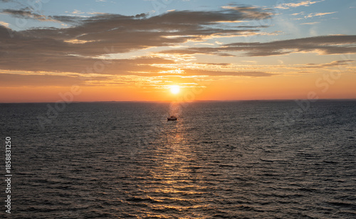 A fishing boat sails in the warm morning sunbeam through the Norwegian Sea at sunrise. Warm morning light shines over the water, creating a bright scene for shrimp fishing.
