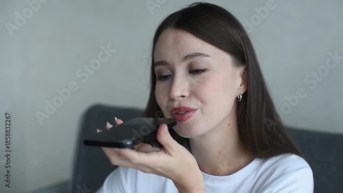 young beautiful caucasian brunette woman recording voice message, smiling widely, casual clothes, white T-shirt, talking by smartphone