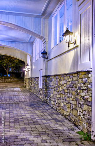 Charming stone wall with warm lantern lighting under an arched entryway at night. Elegant architectural details and cozy ambiance in this inviting, cobblestone-lined outdoor scene.
