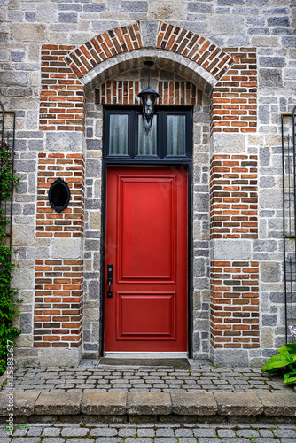 Front view of a vibrant red door set in a rustic brick and stone facade with arched frame and black lantern, showcasing traditional architecture in Old Quebec.