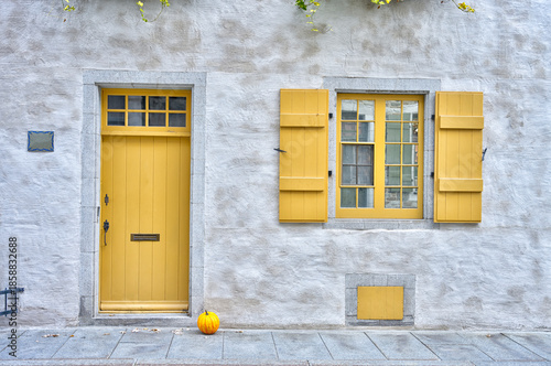 Charming old stone building with a vibrant yellow door and shutters, a small pumpkin at the entrance, evoking a cozy autumn feel. Perfect for themes like architecture, heritage, or seasonal design.