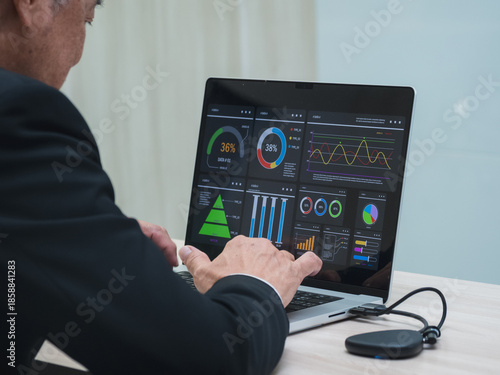 business man in suit analyzing charts and graphs on laptop screen in office setting. image show data visualization such as pie chart and bar graph, representing business analytics and decision-making.