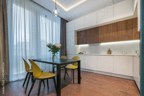 Obraz na płótnie A kitchen space shows a dining table with yellow chairs surrounded by natural light from large windows