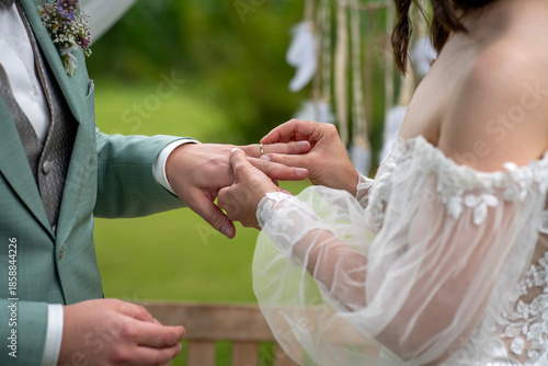 Ringtausch mit dem Anstecken des Ehering durch die Braut beim Bräutigam während der Trauung im Rahmen einer Hochzeit, freie Trauung draußen 