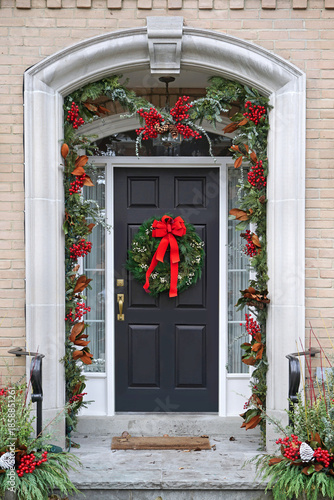 Front door decorated with holly berry and Christmas wreath with red bow