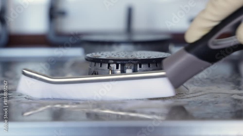 Cleaning process of a stovetop with a brush, showcasing the scrubbing action on the surface, revealing a shiny finish as the brush moves across the grime