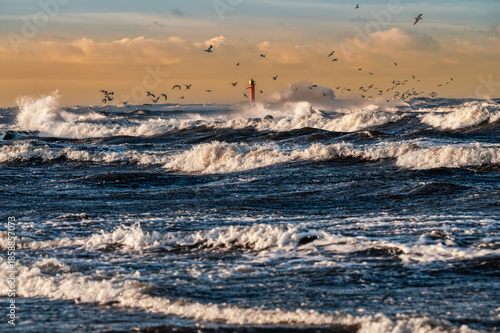 Stormy Baltic Sea with lighthouse and flying birds during rough weather on Mangalsala pier in Riga