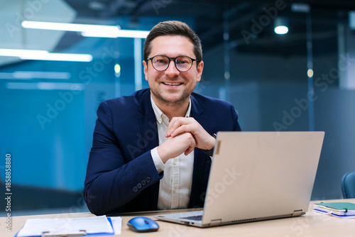 Bild auf Leinwand Charismatic European businessman sitting at desk in stylish office working on la