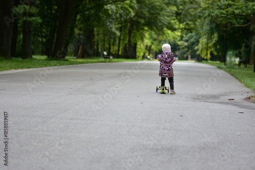 Wallpaper Mural Toddler riding a three-wheel scooter along a park path, back view. Child enjoying freedom, movement and outdoor activity surrounded by green trees and peaceful nature. Torontodigital.ca