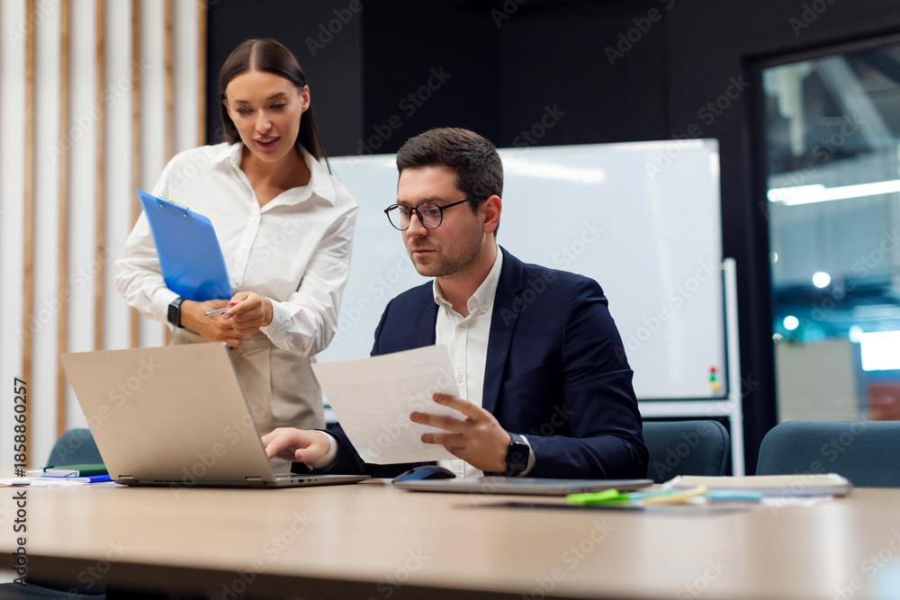 Obraz premium Businessman and businesswoman assistant working with documents, looking at laptop and discussing project during meeting in board room in office, copy space