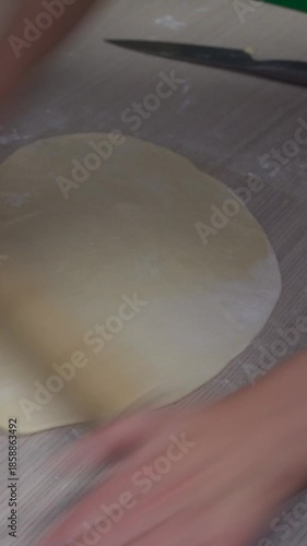 Rolling dough with wooden rolling pin, homemade pastry preparation, close up traditional cooking process on kitchen table, baking and food preparation. 9:16