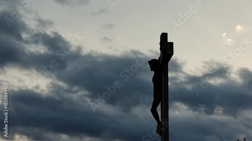 Stone statue representing Jesus Christ crucifixion, at sunset, 4K clouds time lapse