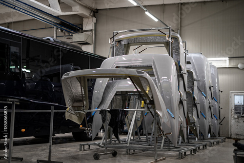 Industrial vehicle manufacturing workshop with metal bus frames and body structures under assembly. Large factory interior shows fabrication, welding, and custom vehicle production in progress.