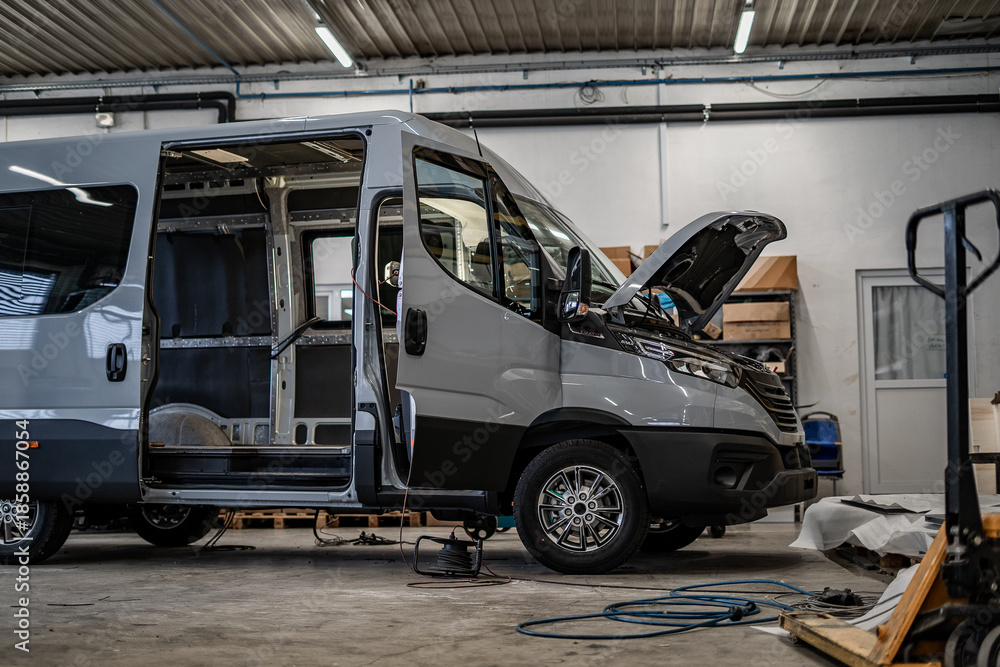 Fototapeta premium Industrial vehicle manufacturing workshop with metal bus frames and body structures under assembly. Large factory interior shows fabrication, welding, and custom vehicle production in progress. 
