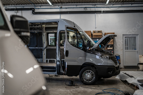 Industrial vehicle manufacturing workshop with metal bus frames and body structures under assembly. Large factory interior shows fabrication, welding, and custom vehicle production in progress.